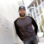 Fashionable bearded man wearing a cap and casual attire in an outdoor urban environment.
